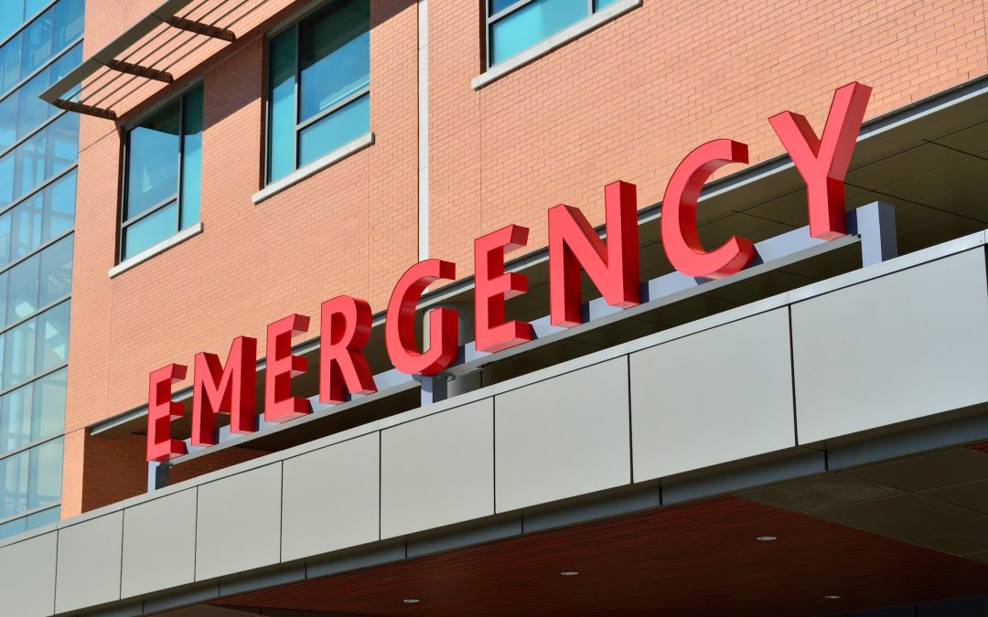 Red "EMERGENCY" sign on the exterior of a brick building, indicating the entrance to a hospital emergency department.