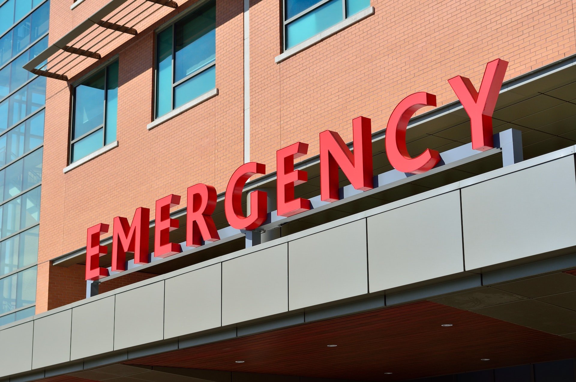 Red "EMERGENCY" sign on the exterior of a brick building, indicating the entrance to a hospital emergency department.