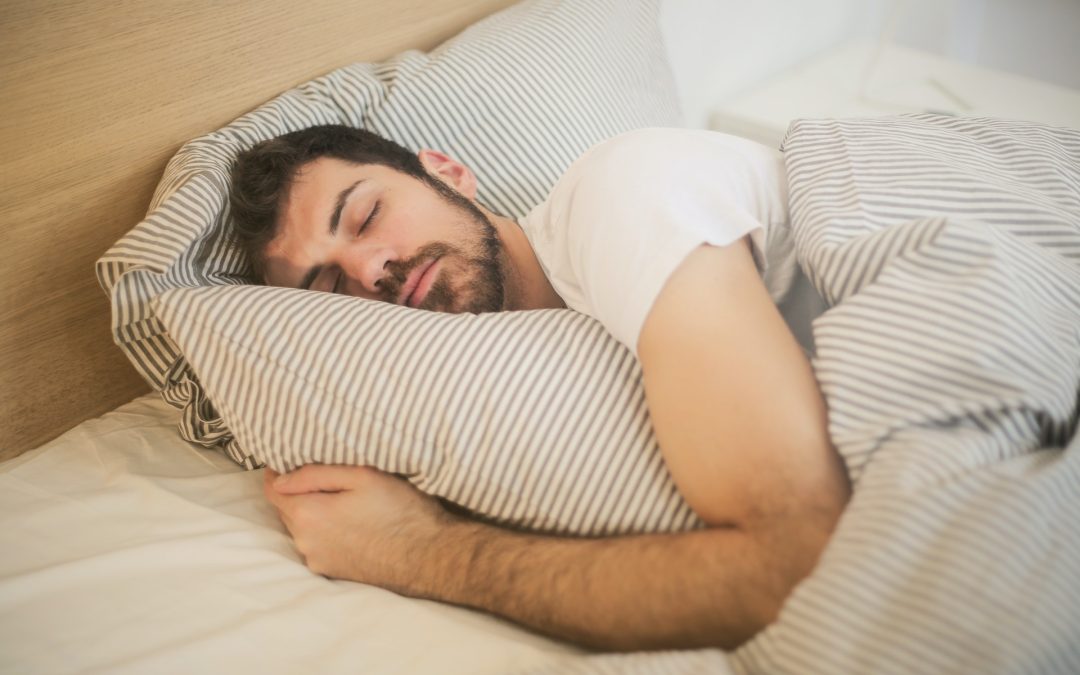 Man sleeping in bed, hugging a striped pillow, covered with a matching striped blanket.