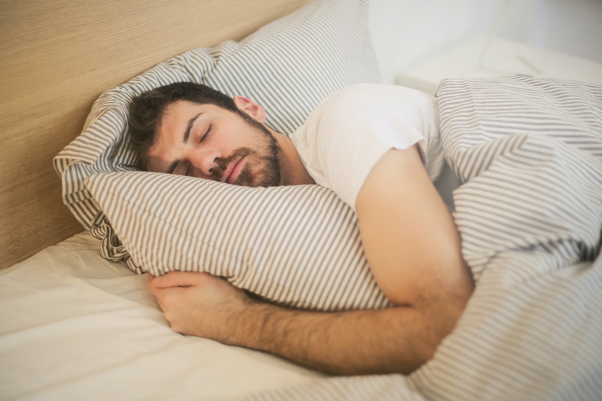 Man sleeping in bed, hugging a striped pillow, covered with a matching striped blanket.