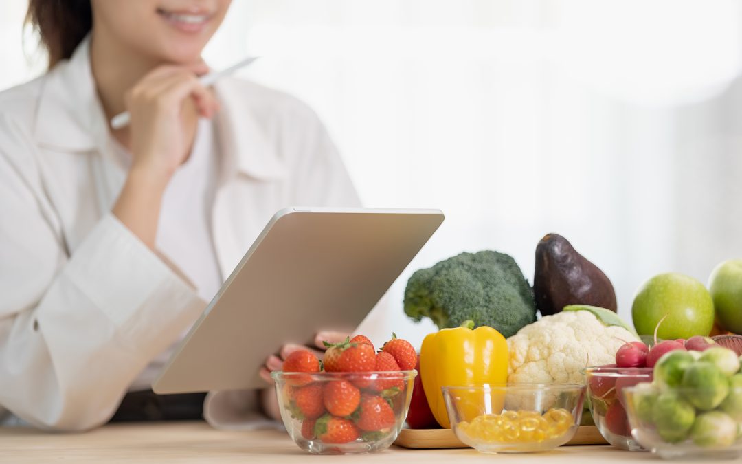 A person holding a tablet near a table with assorted fruits and vegetables, including strawberries and broccoli. Nutrition Counselor